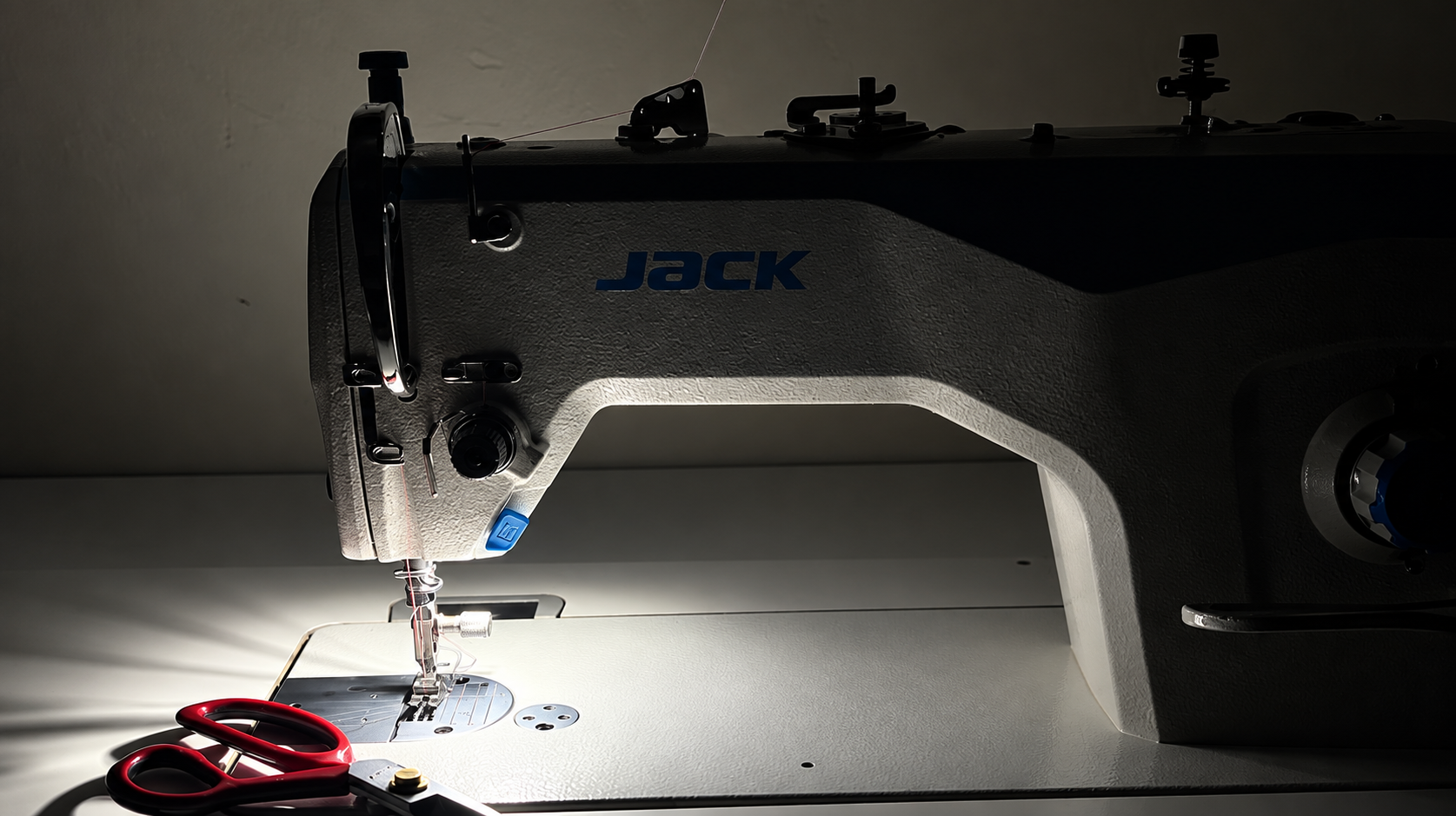 A sewing machine and tailor's shears lit in a dark workroom