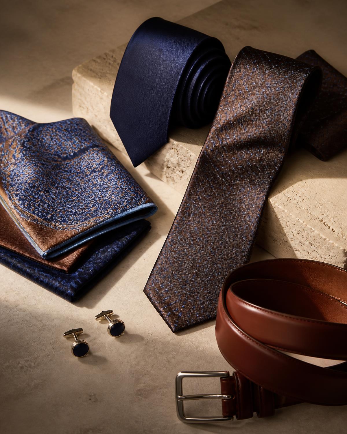 Silk ties, pocket squares, cufflinks and a leather belt on a stone surface